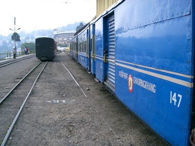 ダージリン鉄道の青い車両が山岳地帯を走る風景。