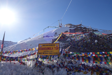 カルドゥン・ラ峠の標高5602mと書いた看板とタルチョの旗