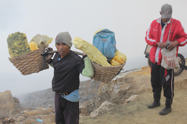 肩に棒を担ぎ両側の竹かごには大量の硫黄の岩石を入れて運び出す労働者