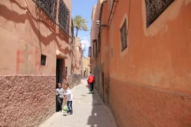 マラケシュの細い路地の両側にオレンジの家の壁が続く風景