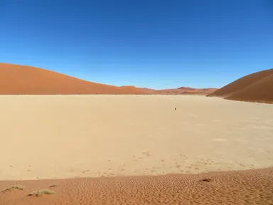 ナミブ砂漠の砂丘に囲まれた場所にあるデッドフレイの白い大地に砂の小さな塊が点在する様子