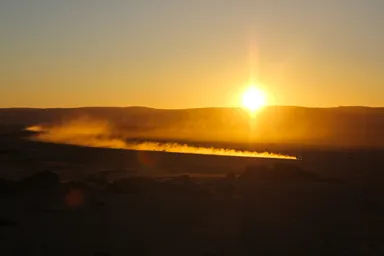 ナミブ砂漠の大地に沈もうとしている夕日と砂煙を上げながら走る車の景色