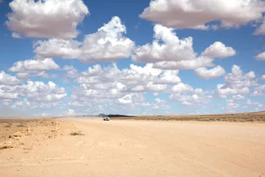 ナミビアの砂の道を砂煙をあげながら走って来る車の様子