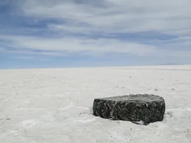 ウユニ塩湖の白一色の世界の中に黒いタイヤが1つある景色