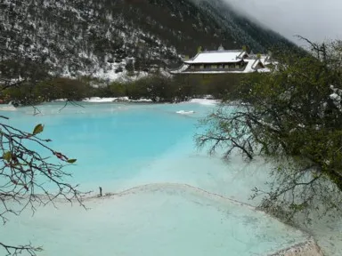真っ青な池の前に立つ雪をかぶったチベット寺院の黄龍古寺