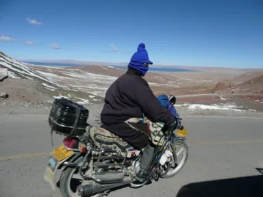 ナムツォの極寒の中を毛布にくるまりバイクを運転する地元民