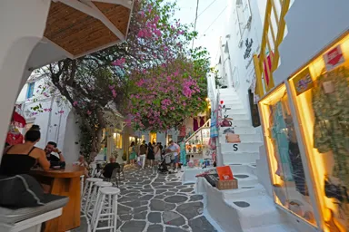 ミコノス島の小さな三差路にお店が並び花が空を埋めて人が集まる光景