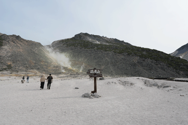 硫黄山アトサヌプリの看板と後ろの煙を上げる白い大地