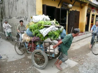 ホイアンの三輪の荷台に大量の荷物を載せて人力で動かす物売りのおじさんの姿